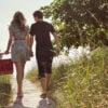 Rear view of couple with holding hands walking on boardwalk amidst field